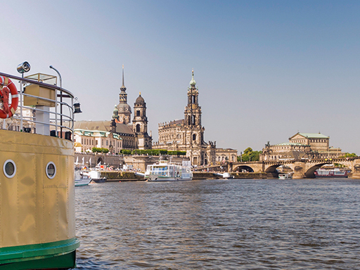 Ein Dampfer fährt auf der Elbe zwischen Augustusbrücke und Carolabrücke. Ein Teil der historischen Silhouette ist zu sehen, dazu ein Motorschiff, das gerade ablegt.