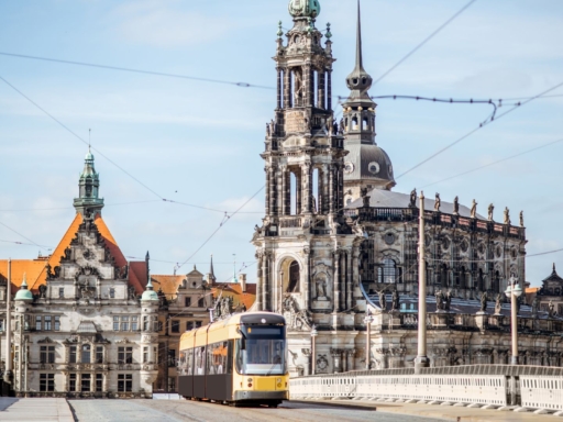 Blick von der Dresdner Neustadt in Richtung Altstadt über die Augustusbrücke. Der Türme der Kathedrale und des Schlosses und das Georgentor prägen das Bild. Eine Straßenbahn führt über die Brücke.