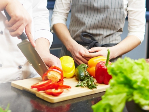 Die Hände eines Kochs der Paprika schneidet. Im Hintergrund die Hände und der Körper einer weiteren Person.