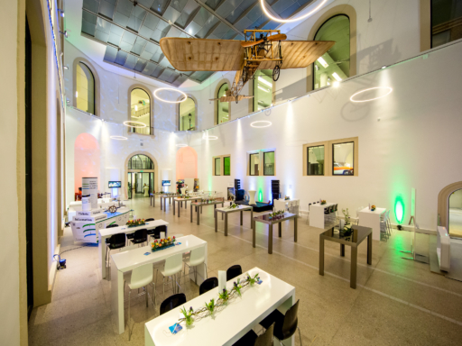 In einem Saal im Verkehrsmuseum stehen eine Reihe von Tischen mit Blumen darauf. An der Decke hängt ein historisches Flugzeug in Originalgröße.