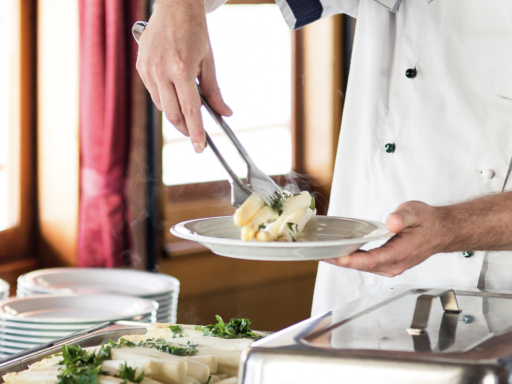 Küchenchef An einem Buffett legt ein Gastromitarbeiter mehrere Stangen weißen Spargel auf einen Teller.