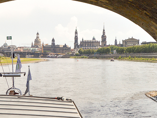 Ein Dampfer fährt stromauf durch die Marienbrücke. Das komplette Panorama der Stadt ist zu sehen - mit Semperoper, dem Turm der Kreuzkirche, dem Hausmannsturm, dem Rathausturm, dem Turm der Kathedrale, dem Turm des Ständehauses, der Frauenkirche und der Kuppel der Kunstakademie.