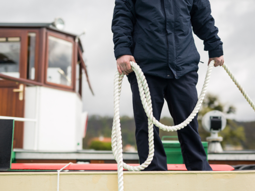 Ein Nautik-Mitarbeiter steht auf einem Schiff und hält eine Leine in der Hand, die beim Anlegen und Festmachen des Schiffs gebraucht wird.