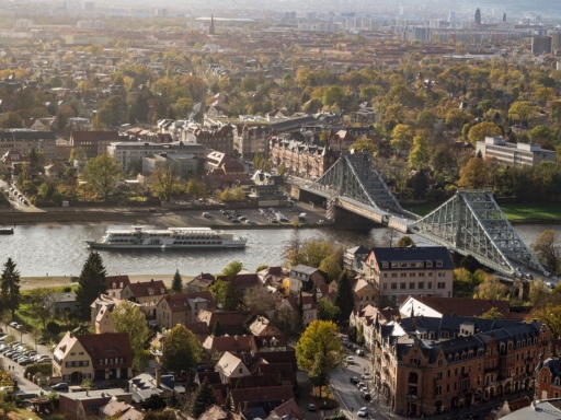 Blick von der Bergstation der Schwebebahn in Dresden auf das Blaue Wunder und die Elbe. Auf dem Fluss fährt ein Salonschiff stromauf. Die Sonne scheint.