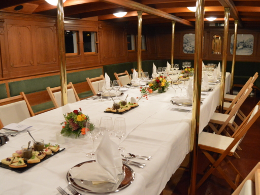 Im Unterdeck-Salon eines Dampfers ist eine lange Tafel eingedeckt. Teller, Gläser und Besteck sind vorbereitet, Blumen und Vorspeisen stehen auf der Tafel.