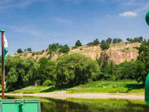 Ein Dampfer fährt stromab und erreicht gerade die Weindörfer Diesbar und Seußlitz. Rechts sind schroffe Felsen zu sehen, davor einige Häuser der zwei Dörfer.