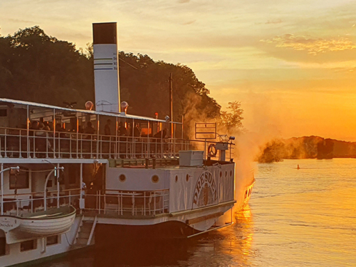 A steamer sails into the sunset. The sky is tinged with orange.