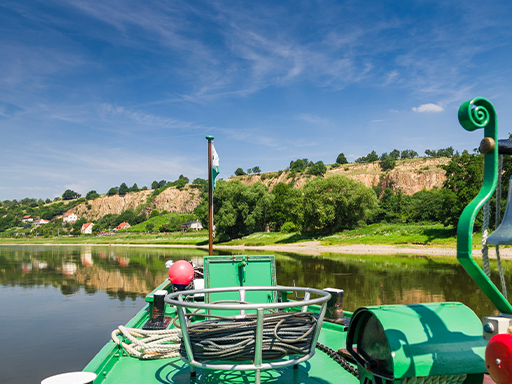 Ein Dampfer fährt stromab und erreicht gerade die Weindörfer Diesbar und Seußlitz. Rechts sind schroffe Felsen zu sehen, davor einige Häuser der zwei Dörfer.