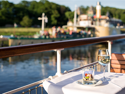 Auf dem Tisch eines Dampfers stehen eine Vorspeise in einem Glas und ein Glas Wein.