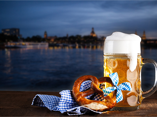 Eine Mass Bier und eine Brezel erinnern vor der Silhouette der Stadt an das Oktoberfest.
