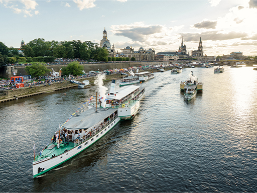Dampfer formieren sich am Terrassenufer zur Flottenparade. Alle pfeifen gemeinsam, aus den Dampfpfeifen steigt weißer Dampf auf.