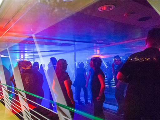Party in einem Salonschiff. Menschen tanzen, blaues Licht beleuchtet die Szenerie.
