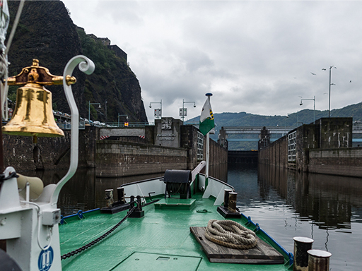 Ein Dampfer fährt in eine Schleuse in Tschechien ein. Im Vordergrund sind der Bug des Schiffs und die goldene Schiffsglocke zu sehen.