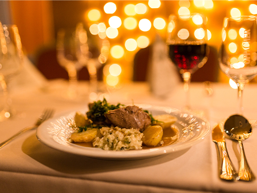 Auf einem festlich gedeckten Tisch steht ein Teller mit einem Hauptgericht. Dahinter stehen mehrere Gläser, unter anderem ein Glas Rotwein.