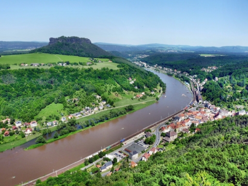 Blick von der Festung Königstein zum Lilienstein und auf den dazwischen liegenden Elbebogen. Unten ist die Stadt Königstein mit der Eisenbahnstrecke zu sehen. Der Himmel ist blau, Es ist Sommer.