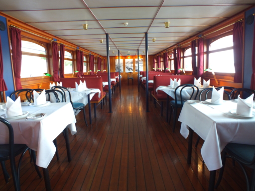Im Decksalon eines Dampfers sind alle Tische mit weißen Tischtüchern, Tellern, Besteck und Servietten eingedeckt.