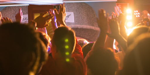 Guests on a ship are having a party. They dance, arms raised in the air. Disco lights illuminate the scene.