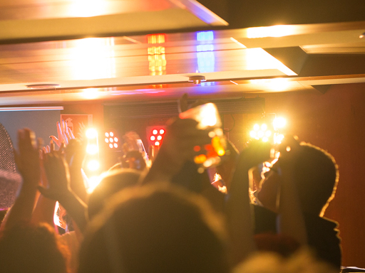 Gäste auf einem Schiff feiern eine Party. Sie tanzen und strecken dabei die Arme nach oben. Diskolicht beleuchtet die Szenerie.