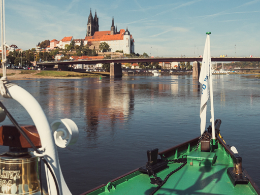 A steamer sails downstream and arrives in Meissen in a few minutes. Ahead is the old Meissen road bridge, and to the left is Albrechtsburg Castle. The sky is blue, and there's no wind.