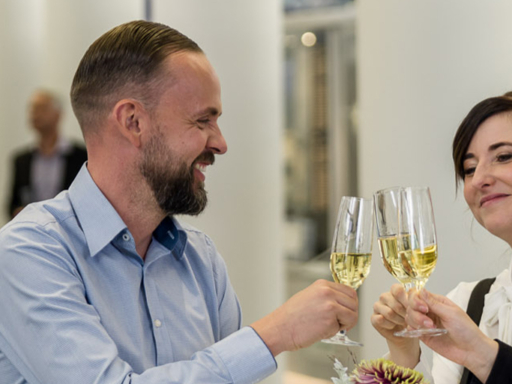 Two women and a man stand at a bar table and clink champagne glasses.