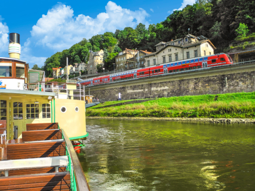 in Dampfer liegt in Königstein. Parallel dazu führt eine S-Bahn auf dem Bahndamm in Richtung Dresden. Es ist sonnig, ein paar weiße Wolken ziehen am Himmel.