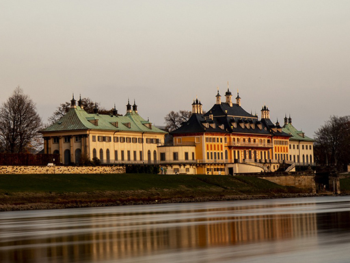 Das Schloss Pillnitz, fotografiert von der anderen Elbseite aus. Die Abendsonne taucht das Schloss in warmes Licht.