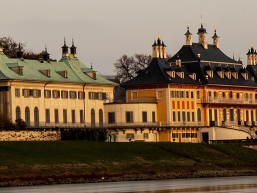 Das Schloss Pillnitz, fotografiert von der anderen Elbseite aus. Die Abendsonne taucht das Schloss in warmes Licht.