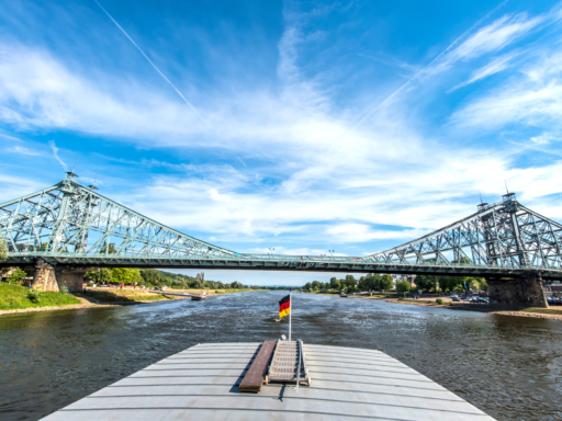 A steamer sails downstream on the Elbe. A view of the ship's stern reveals that it has just passed the Blue Wonder. It's sunny but windy.