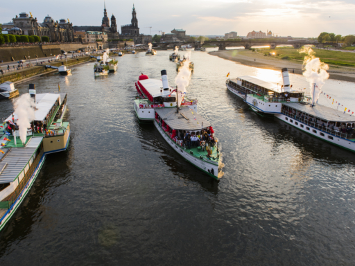 Dampfer formieren sich am Terrassenufer zur Flottenparade. Alle pfeifen gemeinsam, aus den Dampfpfeifen steigt weißer Dampf auf.