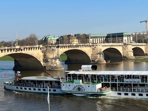Der Dampfer Dresden fährt bei strahlendem Sonnenschein auf der Elbe stromab und passiert gleich die Augustusbrücke. Im Hintergrund ist die Dreikönigskirche zu sehen.