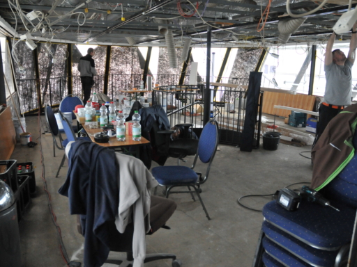 2024-03-22-Umbau Cosel aktueller Stand Fine Dining Club 2 Ein Arbeiter arbeitet an der Decke eines Salonschiff-Raums. Kabel hängen herunter. Im Vordergrund stehen ein Tisch und Stühle für die Pausen der Arbeiter.