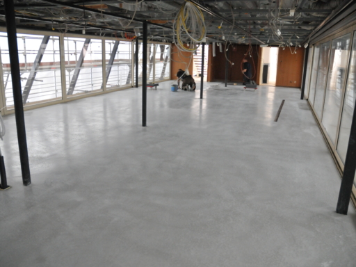 2024-03-22-Umbau Cosel aktueller Stand Lounge Café Im hinteren Teil des Oberdecks in einem Salonschiff ist der neue Fußboden fertig. Die Decke ist noch unverkleidet, es hängen Kabel herunter. Im hinteren Teil des Raums kniet ein Mann und arbeitet am Fußboden.