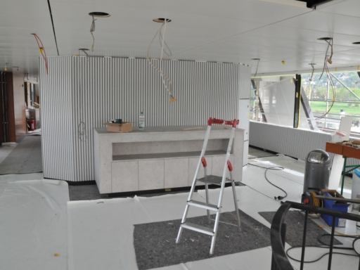 Innenausbau eines Motorschiffs auf der Werft in Laubegast. Erste Wandverkleidungen sind zu sehen, davor ein mobiler Tresen. Von der Decke hängen Kabel dort, wo sich künftig Lampen befinden werden. Der neue Fußboden ist mit Planen geschützt.