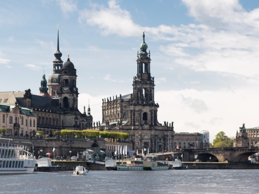 Blick auf die historische Altstadt. Ein Dampfer und ein Salonschiff liegen am Terrassenufer, ein Frachtschiff fährt stromab. Es ist sonnig, aber es gibt auch ein paar Wolken.