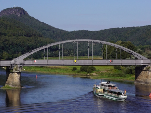 Ein Dampfer fährt auf der Elbe nahe Bad Schandau stromab und unterquert die Eisenbahnbrücke. Der Himmel ist blau, im Hintergrund ist der Lilienstein zu sehen.