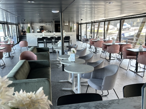 image00008 Ein Blick ins Lounge Café eines Motorschiffs. Bequeme Sofas und Sessel laden zum entspannen ein. Auf den Tischen stehen weiße Blumen in weißen Vasen.