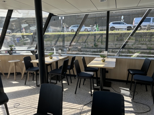 image00021 Blick in die umgestaltete Panorama Bar eines Salonschiffs. Helle Tische und schwarze Stühle sind zu sehen, im Hintergrund durch die Fenster das Terrassenufer.