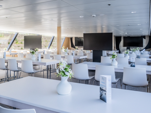 Das Conference Deck im hinteren Teil eines Salonschiffs mit großen Bildschirmen ermöglicht konzentrierte Tagungen. An weißen Tischen stehen jeweils drei bis vier weiße Stühle.