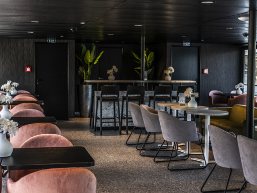Gemütliche Sessel und dunklere Farben prägen das Lounge Café unserer Salonschiffe. Weiße Blumen stehen auf den Tischen.
