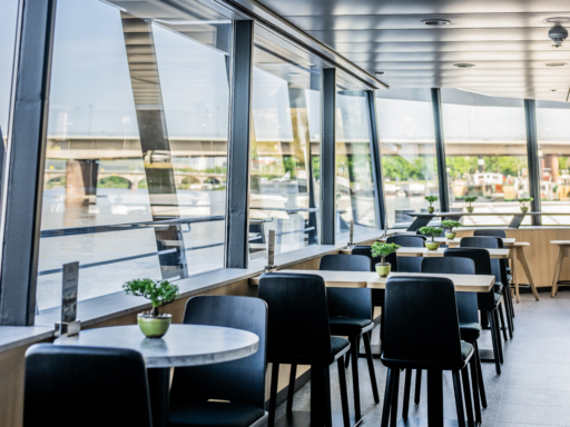 Die Panorama Bar eines Salonschiffs. Mehrer Tische stehen in Reihe, im Hintergrund sind die Top-Plätze hinter der Glasfront des Schiffs zu sehen.