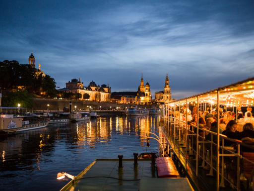 Ein vollbesetzter Dampfer am Abend, nahe des Terrassenufers. Es ist dunkel, die Altstadt und auch der Dampfer sind hell erleuchtet. Im Hintergrund liegen 3 Schiffe am Terrassenufer.