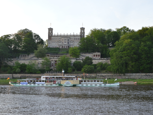 Der Dampfer Pillnitz fährt unterhalb von Schloss Albrechtsberg die Elbe entlang. Es sind bunte Wimpel am Schiff angebracht.