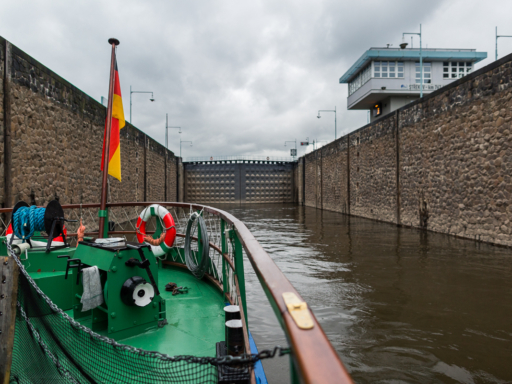 Blick vom Dampfer, Das Schiff steuert in die Schleuse in Ústí nad Labem. Links und rechts des Schiffshecks erstrecken sich hohe Mauern aus Stein, die in ein großes Schleusentor münden.